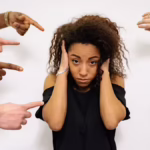 girl with hands over ears wondering how do you handle criticism symbolised by other people's hands pointing at her