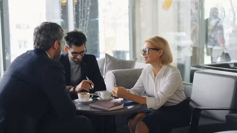 Woman mentoring two men in business leadership over coffee